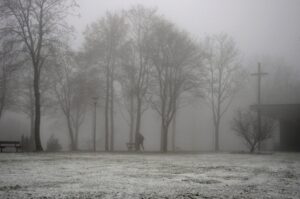 Nebeliger Friedhof in Clausthal-Zellerfeld mit Kreuz und kahlen Bäumen im Winter
