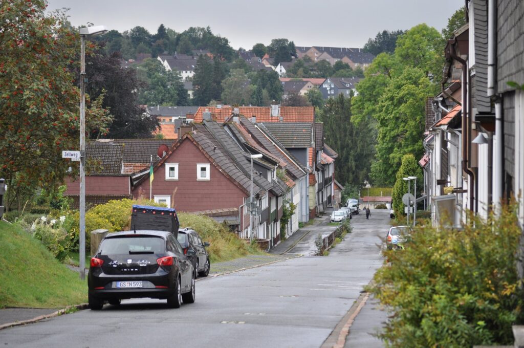 Straße mit Autos in herbstlichem Bergdorf Clausthal-Zellerfeld, Häuser und bewaldete Hügel im Hintergrund
