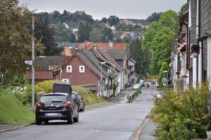Straße mit Autos in herbstlichem Bergdorf Clausthal-Zellerfeld, Häuser und bewaldete Hügel im Hintergrund